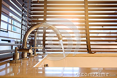 Close up ofÂ water flow from water tap into bathtub with wooden venetian blinds on background in bathroom Stock Photo